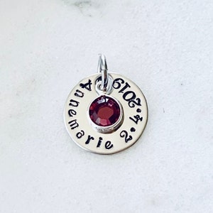 May include: Silver charm with a red gemstone and the text "Annemarie 2.14.2016" engraved on it.