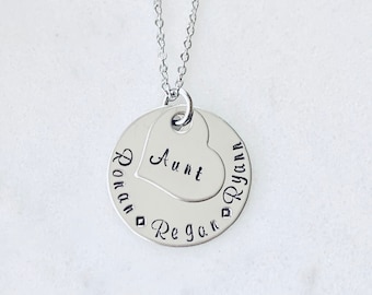 Puede incluir: Collar de plata con un colgante redondo que dice "Tía" dentro de una forma de corazón. El colgante también dice "Ryan Regan" alrededor del exterior.