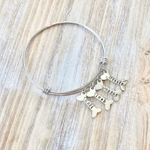 May include: Silver charm bracelet with four dog bone charms, each engraved with a different name: Kali, Tank, Roscoe, and Minnie.