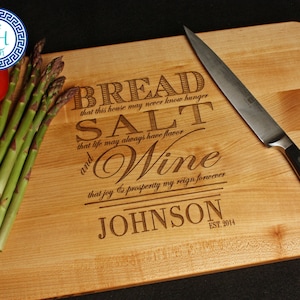 May include: A wooden cutting board with engraved text that reads "Bread, Salt, and Wine." A knife, tomato, and asparagus are on the board. The text includes the family name "Johnson" and the year "2014".