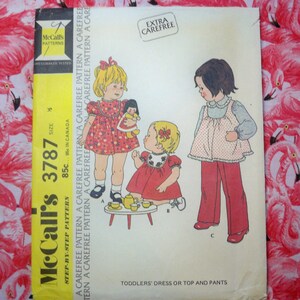 May include: A vintage McCall's sewing pattern for toddlers' dress or top and pants. The pattern number is 3787 and the price is 85 cents. The pattern features a girl in a red dress with a white collar and a girl in a blue top with red pants.