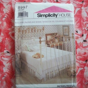 May include: A Simplicity House sewing pattern for bedcovers, pillows, and shams. The pattern number is 8997 and the size is one size. The pattern shows a white bed with a white bedspread and a white ruffled bed skirt. The bed has a brass headboard and footboard.