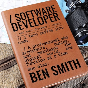 Peut inclure: Un carnet en cuir marron avec l'inscription "SOFTWARE DEVELOPER" en noir. Le carnet contient une définition et le nom "BEN SMITH". Un appareil photo et une carte sont visibles en arrière-plan. Le carnet est de taille A5, environ 14,8 x 21 cm.