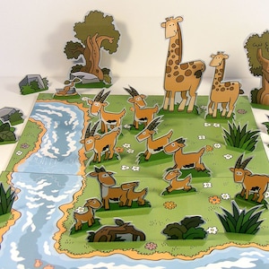 May include: A paper craft set featuring a river, trees, and animals. The set includes a giraffe, a smaller giraffe, and several brown and white gazelles. The animals are all standing on a green grassy field with white flowers.