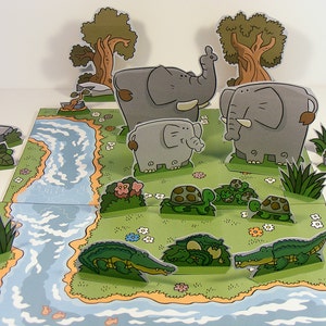 May include: A pop-up book with a jungle theme featuring a river, trees, elephants, and turtles. The book is made of paper and has a colorful design.