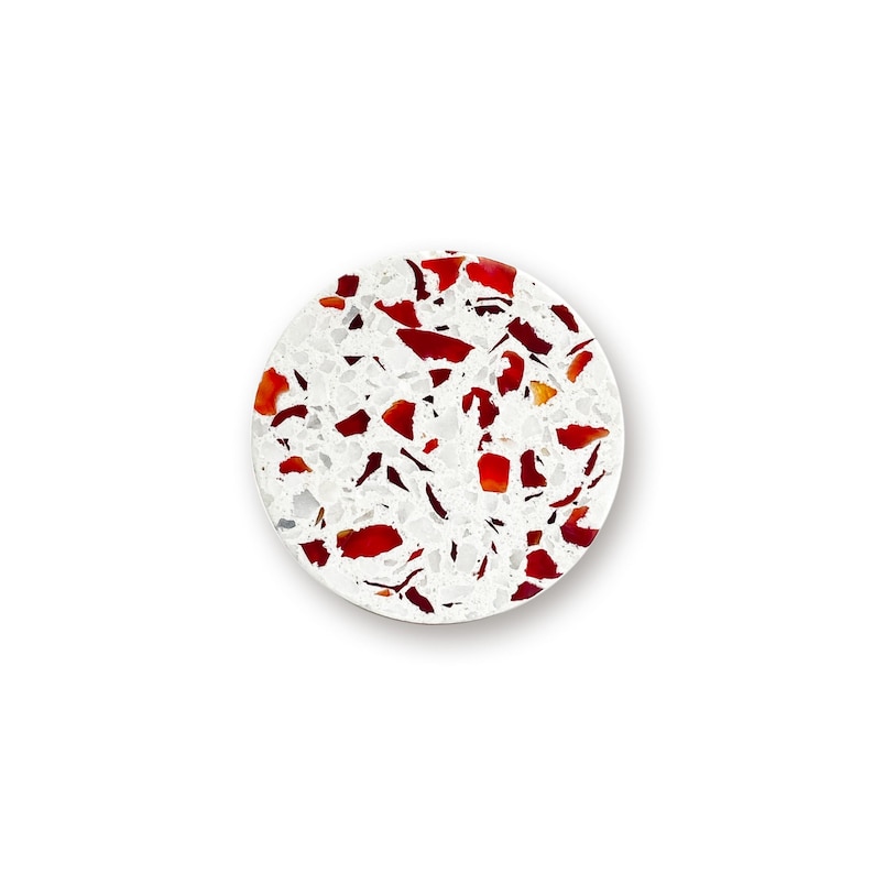May include: A circular coaster featuring a white base embedded with numerous irregular, scattered red and dark red fragments. The surface has a speckled, terrazzo-like appearance with a smooth finish, creating a high-contrast pattern of white and red.