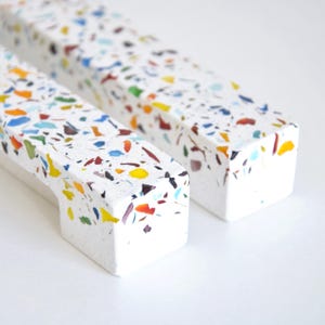 Può includere: Due maniglie per mobili rettangolari con base bianca e macchie colorate in stile terrazzo. Una maniglia ha un'apertura curva per la maniglia. Le maniglie sono realizzate in materiale solido.