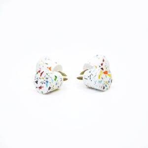 May include: Four white cabinet knobs with a multicolored terrazzo pattern featuring flecks of blue, green, orange, and brown. Each knob has a conical shape and includes a metal screw attached to the back for installation on furniture or doors.