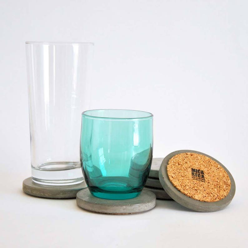 Puede incluir: Tres posavasos de hormig&oacute;n gris con una parte superior de corcho. La parte superior de corcho tiene el texto "BRICK RIG" impreso. Dos vasos de vidrio transparente y un vaso de vidrio turquesa est&aacute;n sobre los posavasos.