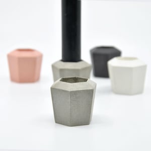 Può includere: Cinque portacandele in cemento geometrici in vari colori, tra cui grigio, rosa, bianco e nero. I portacandele sono tutti esagonali e hanno una superficie ruvida e testurizzata.