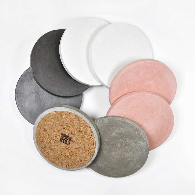 Puede incluir: Conjunto de ocho posavasos redondos en varios colores, incluyendo gris, blanco y rosa. Algunos posavasos tienen un respaldo de corcho. Un posavasos tiene el texto "Since Rica" impreso en &eacute;l.