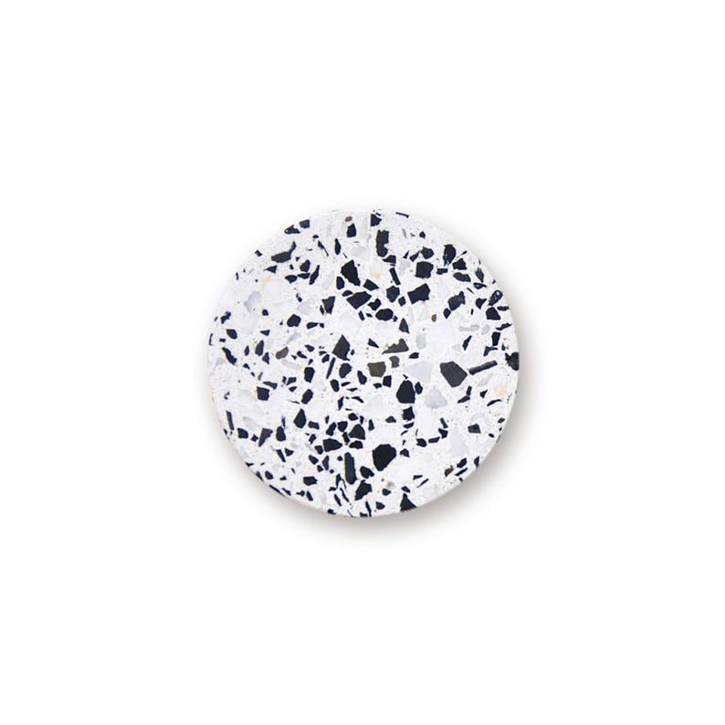 May include: A circular coaster featuring a white base with a scattered pattern of black and dark gray angular stone chips. The surface has a speckled terrazzo appearance with a smooth finish and a clean, defined edge against a plain white background.