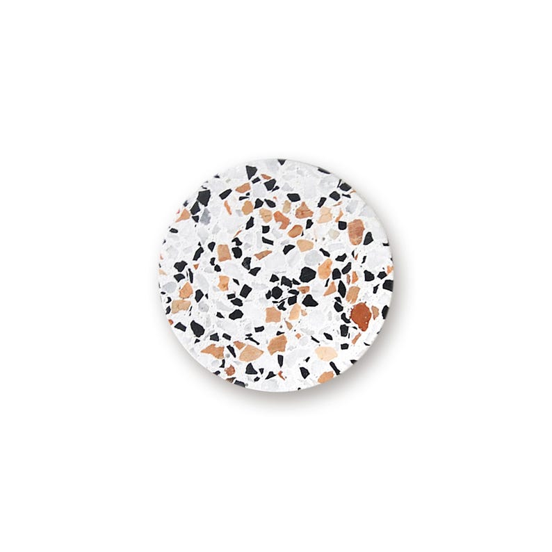 May include: A circular coaster featuring a white base with a scattered terrazzo pattern. The surface is embedded with various angular chips in shades of black, light gray, and warm terracotta brown, creating a multi-colored speckled appearance.