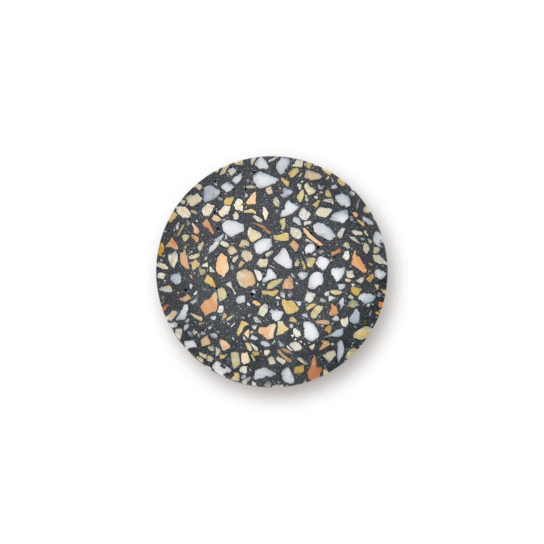 May include: A circular coaster featuring a dark charcoal gray base embedded with a dense pattern of multi-colored stone chips in shades of white, cream, tan, and light orange, creating a speckled terrazzo effect across the entire flat surface.