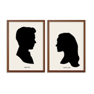 May include: Two framed art prints featuring black silhouette profiles against a cream background. One print reads "MIKE ROSS" at the bottom. The other print features a woman's silhouette and reads "RACHEL ZANE". The frames are a dark brown color.