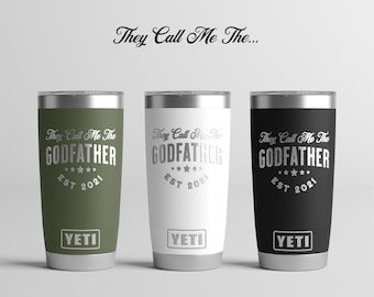 May include: Three stainless steel tumblers with a silver lid and base. The tumblers are green, white, and black. Each tumbler has the text "They Call Me The GODFATHER EST 2021" and the word "YETI" printed on the bottom.