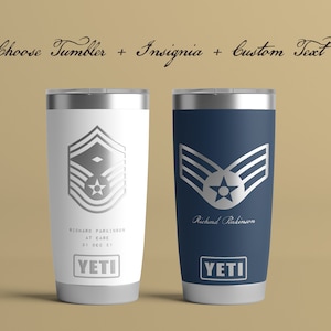 May include: Two stainless steel YETI tumblers with a silver insignia of an Air Force rank and a personalized name. The tumbler on the left is white and the tumbler on the right is blue.