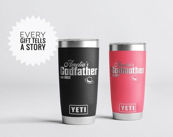 May include: Two stainless steel YETI tumblers with black and pink lids. The black tumbler has "Amelia's Godfather est 2022" engraved on it. The pink tumbler has "Amelia's Godmother est 2022" engraved on it.