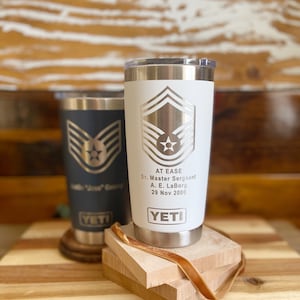 May include: Two stainless steel YETI tumblers with a white background and a silver Air Force Master Sergeant rank insignia. The text "AT EASE" is engraved on the white tumbler, along with "Sr. Master Sergeant", "A. E. LaBorg", and "29 Nov 2000".