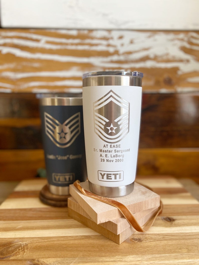 May include: Two stainless steel YETI tumblers with a white background and a silver Air Force Master Sergeant rank insignia. The text "AT EASE" is engraved on the white tumbler, along with "Sr. Master Sergeant", "A. E. LaBorg", and "29 Nov 2000".