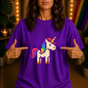 Peut inclure: Un t-shirt violet avec un motif de licorne pixélisée. La licorne a une crinière et une queue arc-en-ciel, et une corne jaune. Le t-shirt est de couleur violet uni.