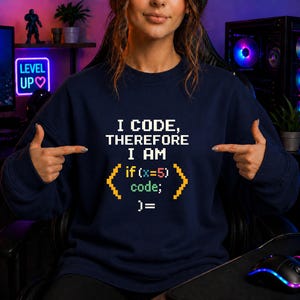 Könnte beinhalten: Marineblaues Sweatshirt mit dem Text "I CODE, THEREFORE I AM" in weißer Pixel-Schrift. Darunter wird der Codeausschnitt "if (x=5) code; )=" in Gelb und Grün angezeigt.