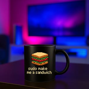 Könnte beinhalten: Schwarze Kaffeetasse mit einem pixeligen Sandwich-Design und dem Text "sudo make me a sandwich". Die Tasse steht auf einer dunkelbraunen Oberfläche. Der Hintergrund ist unscharf.