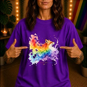 Könnte beinhalten: Ein violettes T-Shirt mit einer Aquarell-Illustration eines Fuchses, der von einem lebendigen, regenbogenfarbenen Spritzeffekt umgeben ist. Unter dem Fuchs steht der Text "LOVE HAS NO LIMITS", ergänzt durch ein kleines Regenbogen-Herz-Symbol.
