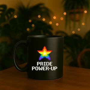 Könnte beinhalten: Schwarze Keramik-Tasse mit einem pixeligen Stern in Regenbogenfarben. Auf der Tasse steht in weißen Buchstaben "PRIDE POWER-UP". Die Tasse steht auf einer Holzoberfläche.