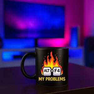 Könnte beinhalten: Schwarze Keramik-Tasse mit Henkel. Die Tasse zeigt ein pixeliges Design von Flammen, den Tasten ALT und F4 sowie den Text "MY PROBLEMS" in Gelb. Die Tasse steht auf einer dunklen Oberfläche.