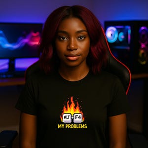 Könnte beinhalten: Schwarzes T-Shirt mit einem pixeligen Design der Alt- und F4-Tasten in Flammen, darunter der Text "MY PROBLEMS". Die Grafik verwendet Rot-, Orange- und Gelbtöne. Das T-Shirt wird von einer Person mit dunklem Haar getragen.