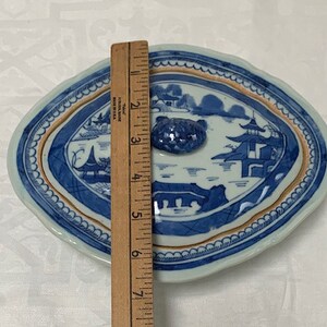 May include: A blue and white porcelain oval serving dish with a lid. The dish features a Chinese landscape scene with a pagoda and a river. The lid has a knob in the shape of a flower.