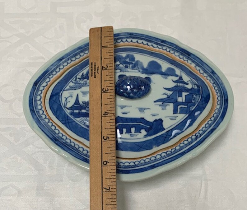 May include: A blue and white porcelain oval serving dish with a lid. The dish features a Chinese landscape scene with a pagoda and a river. The lid has a knob in the shape of a flower.
