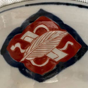 Op de afbeelding: Een close-up van een rood en wit keramisch ontwerp op een wit bord. Het ontwerp heeft een gestileerd blad en een swirl-patroon.