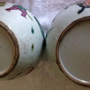 May include: Two white porcelain bowls with a brown rim. The bowls are decorated with colourful painted figures and flowers.
