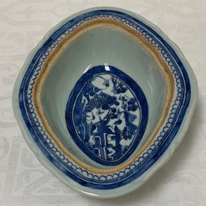 May include: A blue and white porcelain bowl with a scalloped rim and a central oval design featuring a landscape scene. The bowl has a brown rim and a white interior.