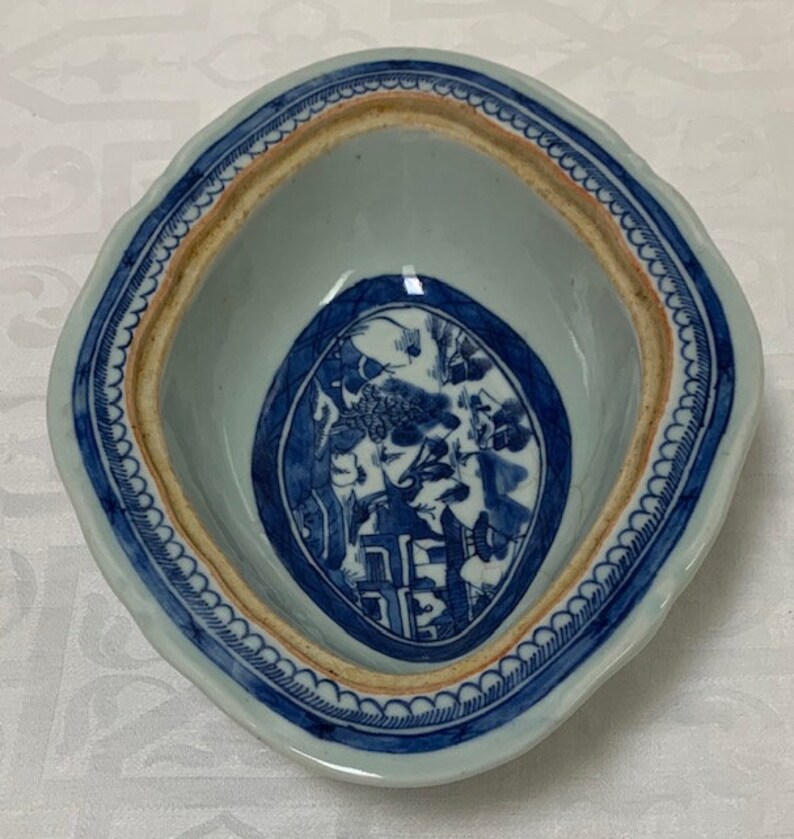 May include: A blue and white porcelain bowl with a scalloped rim and a central oval design featuring a landscape scene. The bowl has a brown rim and a white interior.