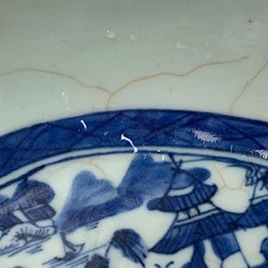 May include: A blue and white porcelain bowl with a decorative design of a Chinese landscape scene. The bowl has a crackle glaze and a blue rim.