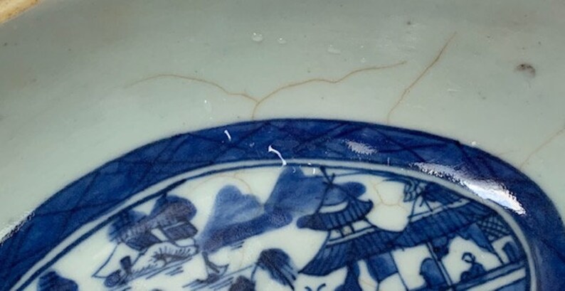May include: A blue and white porcelain bowl with a decorative design of a Chinese landscape scene. The bowl has a crackle glaze and a blue rim.