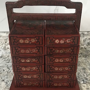 May include: A red wooden stacking box set with a decorative handle. The boxes are decorated with floral patterns and a black and white geometric design.
