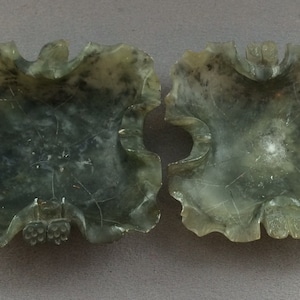 May include: Two antique green jadeite stone dishes with intricate carved designs. The dishes are in the shape of a four-leaf clover and have a smooth, polished finish.