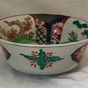 Op de afbeelding: Een witte keramische kom met een brede rand en een bloemenmotief in tinten rood, groen, blauw en zwart. De kom heeft een traditionele Japanse stijl.