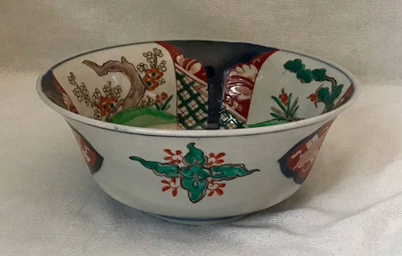 Op de afbeelding: Een witte keramische kom met een brede rand en een bloemenmotief in tinten rood, groen, blauw en zwart. De kom heeft een traditionele Japanse stijl.