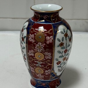 May include: A small, red and blue porcelain vase with a floral pattern. The vase has a gold trim and is decorated with a variety of flowers and leaves.