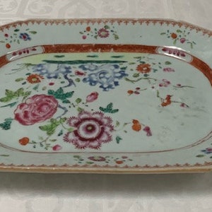 Könnte beinhalten: Eine große, ovale Servierplatte aus Porzellan mit einer hellblauen Glasur und einem Blumendesign in den Farben Rosa, Rot, Grün und Blau. Die Platte hat einen gewellten Rand und einen erhöhten Rand.