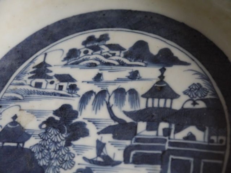 K&ouml;nnte beinhalten: Ein blauer und wei&szlig;er Porzellanteller mit einem traditionellen chinesischen Landschaftsdesign. Die Szene zeigt eine Pagode, H&auml;user, B&auml;ume und einen Fluss. Der Teller ist mit einer blauen und wei&szlig;en Glasur verziert.