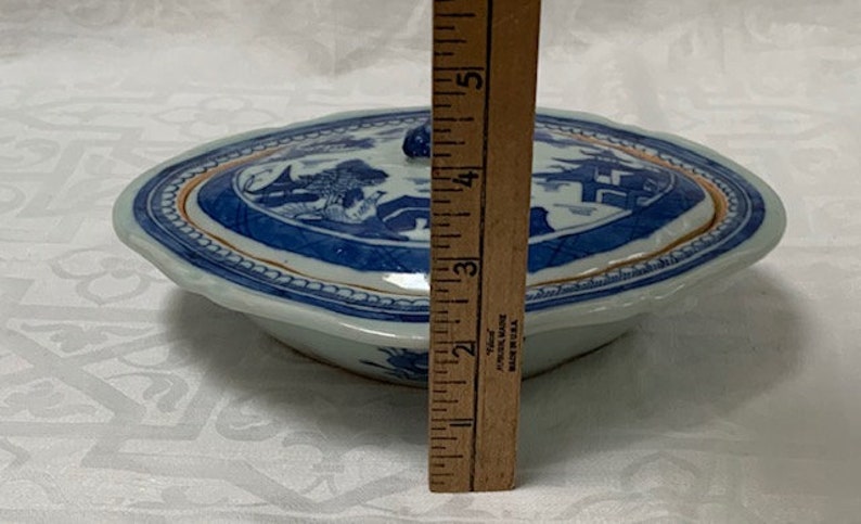 May include: A blue and white porcelain serving dish with a lid. The dish has a scalloped edge and a gold trim. The lid has a knob on top. The dish is 5 inches in diameter.