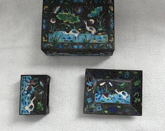 May include: A set of three small, square, black boxes with blue and green enamel designs. The boxes feature a floral pattern with birds and are decorated with intricate details.