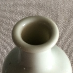 Może przedstawiać: Biały ceramiczny wazon z szerokim otworem. Wazon ma gładkie, błyszczące wykończenie.