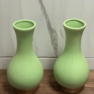 Può includere: Due vasi in ceramica verde chiaro con un bordo dorato. I vasi sono rotondi e hanno un collo stretto.